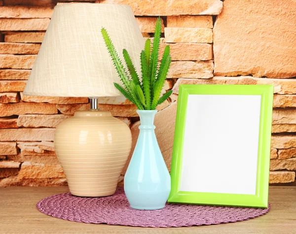 Marco de fotos colorido, lámpara y flores en la mesa de madera sobre fondo de pared de piedra — Foto de Stock