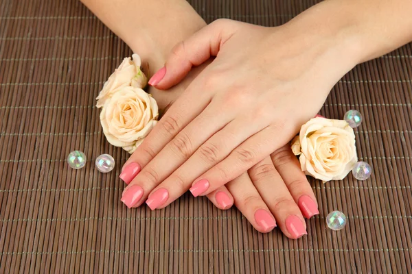 Manos de mujer con manicura rosa y flores, sobre fondo de estera de bambú —  Fotos de Stock