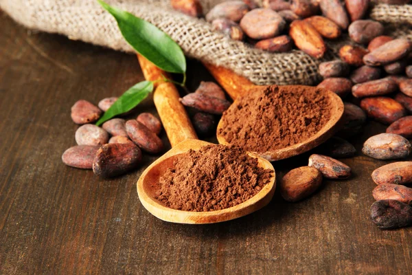 Cacao en polvo en cucharas y granos de cacao sobre fondo de madera —  Fotos de Stock