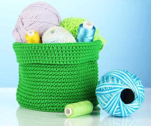 Colorful yarn for knitting in green basket on blue background — Stock Photo, Image