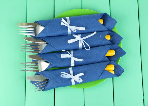 Forks and knives wrapped in blue paper napkins, on color wooden background — Stock Photo, Image