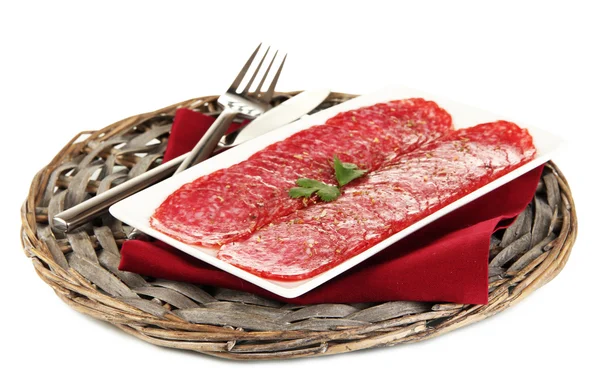 Tasty salami on plate on wicker cradle isolated on white — Stock Photo, Image