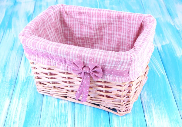 Wicket basket with pink fabric and bow, on color wooden background — Stock Photo, Image