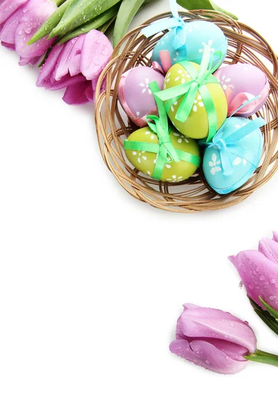 Huevos de Pascua brillantes en cesta y tulipanes, aislados en blanco — Foto de Stock