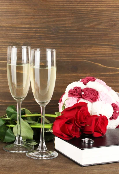 Snubní prsteny na Bibli s růžemi a sklenic šampaňského na dřevěné pozadí — Stock fotografie