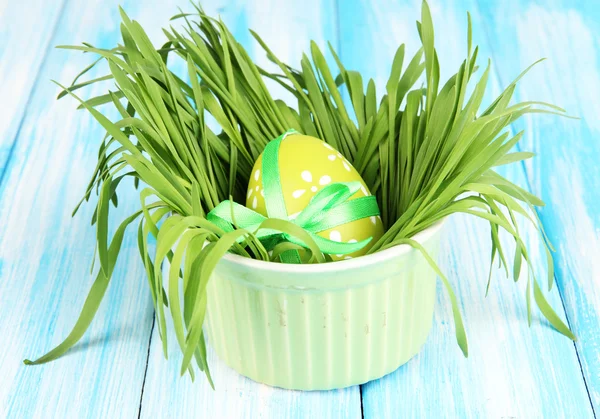 Easter egg in bowl with grass on blue wooden table close up — Stock Photo, Image