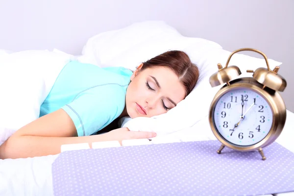 Vacker ung kvinna som sover på sängen med väckarklocka i sovrum — Stockfoto