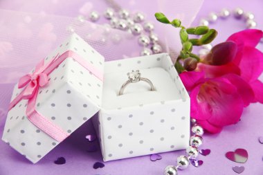 Beautiful box with wedding ring and flower on purple background clipart