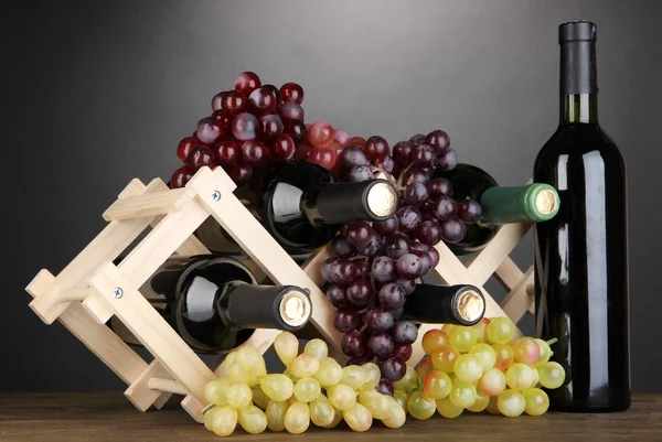 Бутылки вина помещены на деревянный стенд на сером фоне — стоковое фото