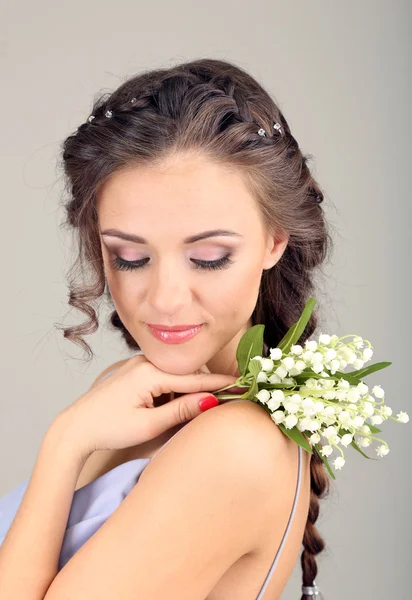 Jovem com belo penteado e flores, em fundo cinza — Fotografia de Stock