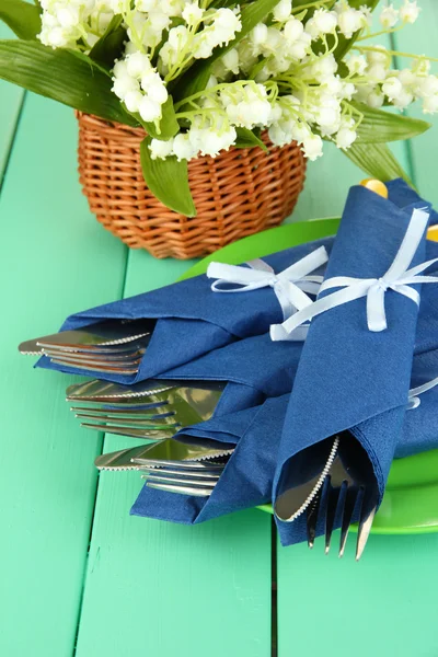 Fork and knife wrapped in blue paper napkin, on color wooden background — Stock Photo, Image
