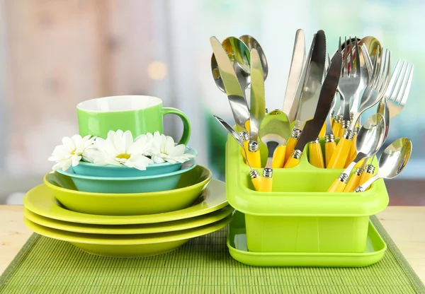 Plates, forks, knives, spoons and other kitchen utensil on bamboo mat, on bright background — Stock Photo, Image