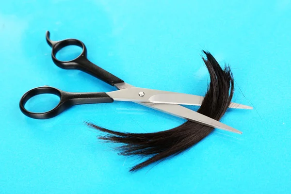 Pedaços de cabelo cortados com tesoura em fundo azul — Fotografia de Stock