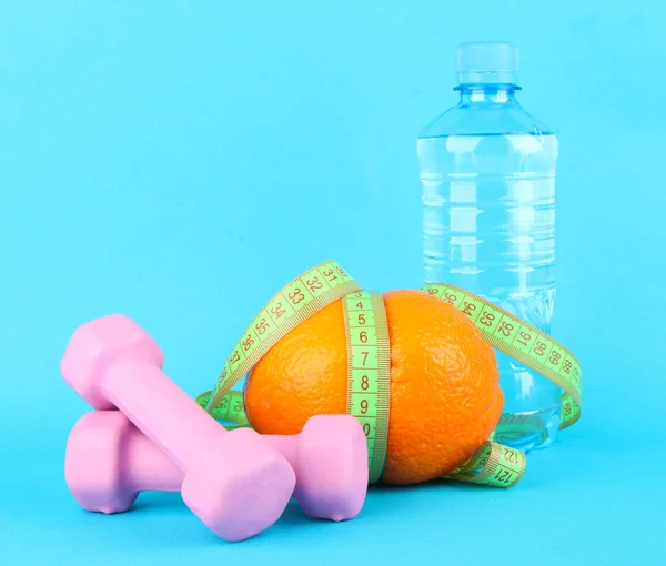 Orange with measuring tape, dumbbells and bottle of water, on color background — Stock Photo, Image