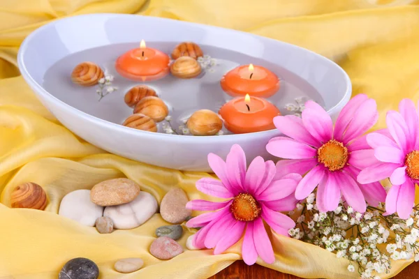 Beautiful candles swim in beautiful plate on yellow fabric close-up — Stock Photo, Image