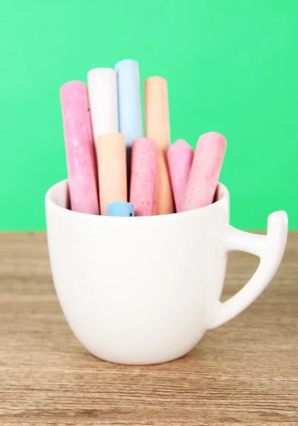 Colorful chalks in cup on table on green background — Stock Photo, Image