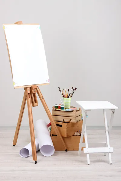 Деревянный мольберт с чистой бумагой и художественными принадлежностями в номере — стоковое фото