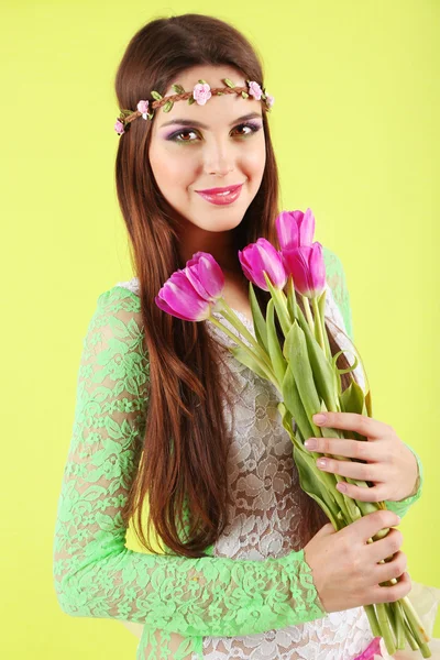 Young beautiful girl with decorative wreath on her head holding bouquet of flowers, on green background — Stock Photo, Image