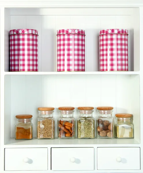 Beautiful white shelves with spices in glass bottles — Stock Photo, Image