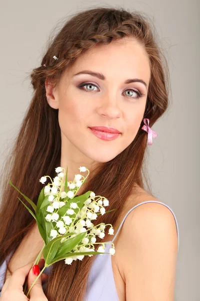 Mujer joven con hermoso peinado y flores, sobre fondo gris —  Fotos de Stock