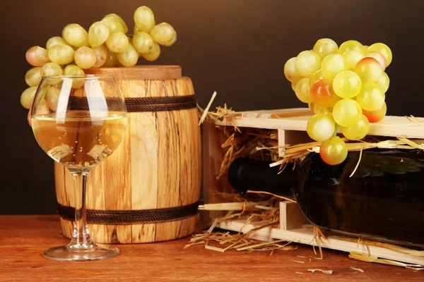 Wooden case with wine bottle, barrel, wineglass and grape on wooden table on brown background — Stock Photo, Image