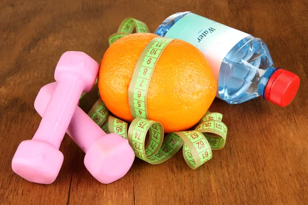 Orange with measuring tape,dumbbells and bottle of water, on wooden background — Stock Photo, Image