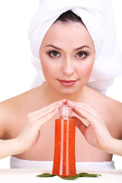 Mulher bonita com toalha na cabeça e garrafa de creme com esfoliação isolada em branco — Fotografia de Stock