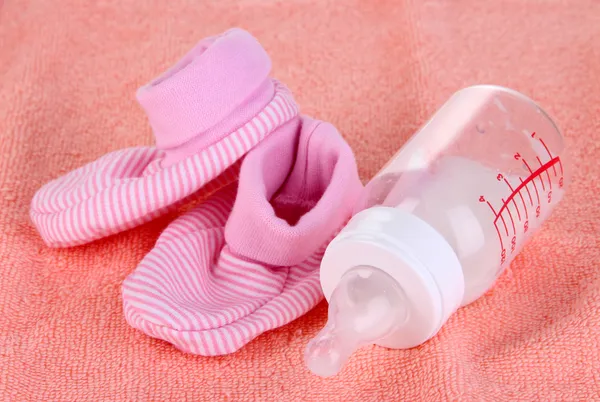 Bottle for milk and booties on pink towel background — Stock Photo, Image