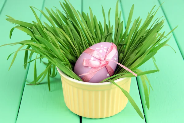 Uovo di Pasqua in ciotola con erba su tavolo di legno verde da vicino — Foto Stock