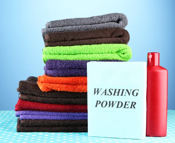 Pile of colorful towels, wash powder and bottle of conditioner for laundry, on blue background — Stock Photo, Image
