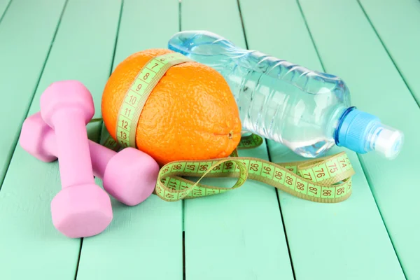 Orange with measuring tape, dumbbells and bottle of water, on color wooden background — Stock Photo, Image