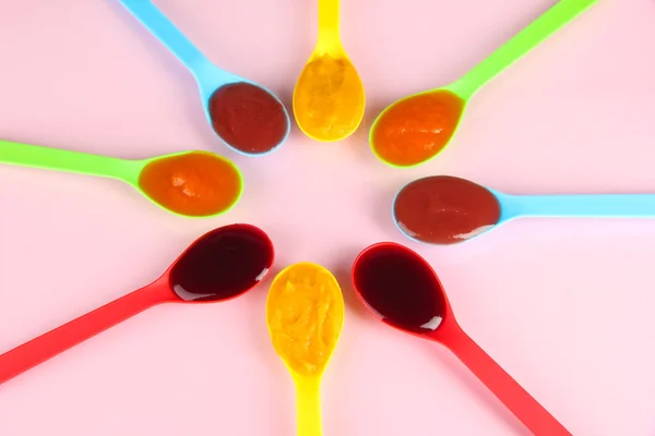 Puré de bebé en cucharas sobre fondo rosa — Foto de Stock