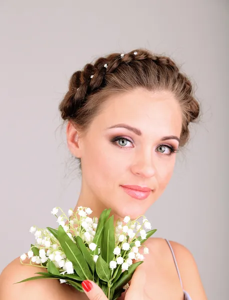 Молодая женщина с красивой прической и цветами, на сером фоне — стоковое фото