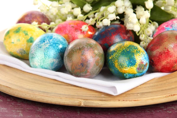 Huevos de Pascua en plato de madera en servilleta con flores de cerca —  Fotos de Stock