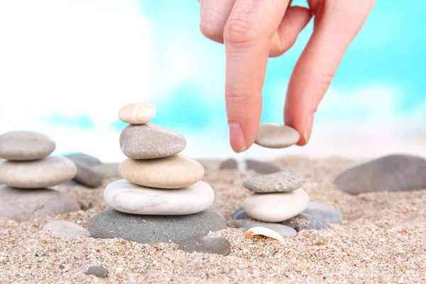 Ręcznie buduje wieżę kamienie morze na piasku na jasnym tle — Zdjęcie stockowe