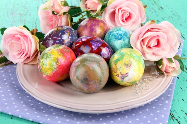 Œufs de Pâques sur assiette avec serviette et fleurs sur table en bois — Photo