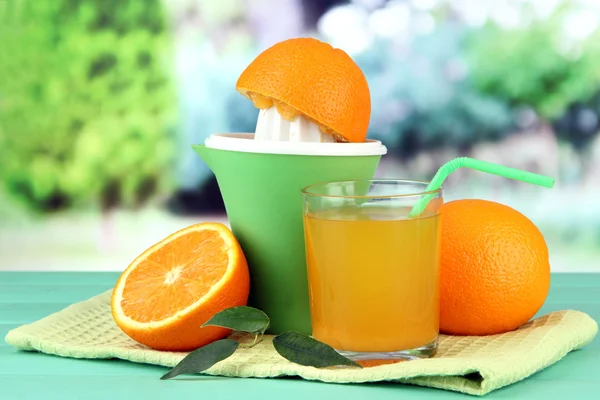 Wyciskarka do cytrusów, kieliszek soku i dojrzałych pomarańczy na zielony Stół drewniany — Zdjęcie stockowe