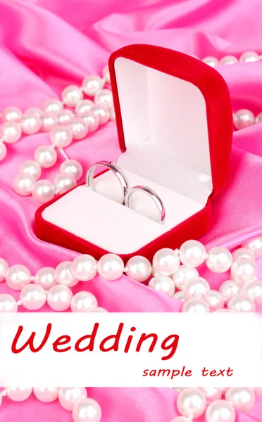Anillos de boda en caja roja sobre fondo de tela rosa — Foto de Stock