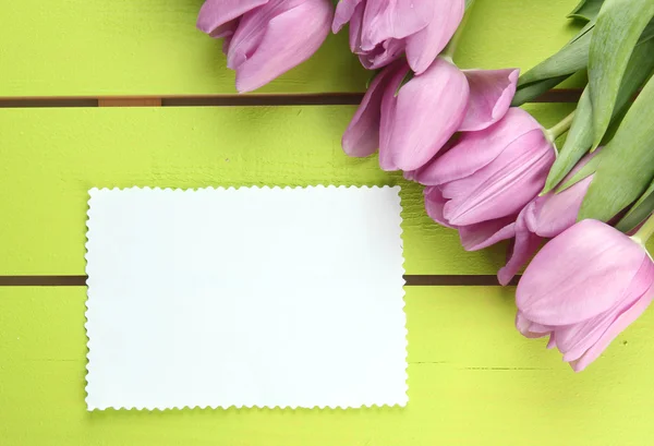 Beautiful bouquet of purple tulips and blank card on green wooden background — Stock Photo, Image