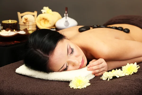 Beautiful young woman in spa salon with spa stones, on dark background — Stock Photo, Image