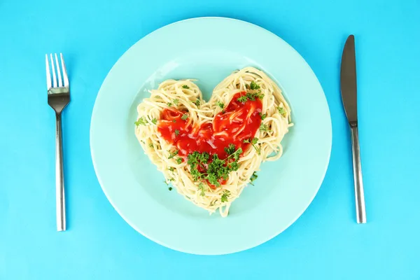 Cooked spaghetti carefully arranged in heart shape and topped with tomato sauce, on color background