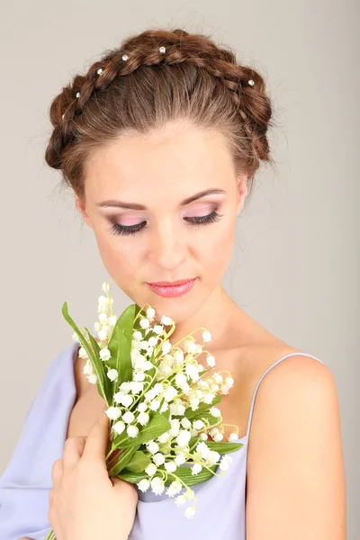 Mujer joven con hermoso peinado y flores, sobre fondo gris —  Fotos de Stock