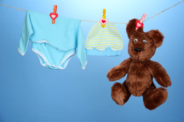 Babykleidung hängt an der Wäscheleine, auf blauem Hintergrund — Stockfoto