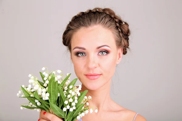 Giovane donna con bella acconciatura e fiori, su sfondo grigio — Foto Stock