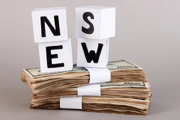 Cubos de papel blanco etiquetados como "Noticias" con dinero sobre fondo gris —  Fotos de Stock