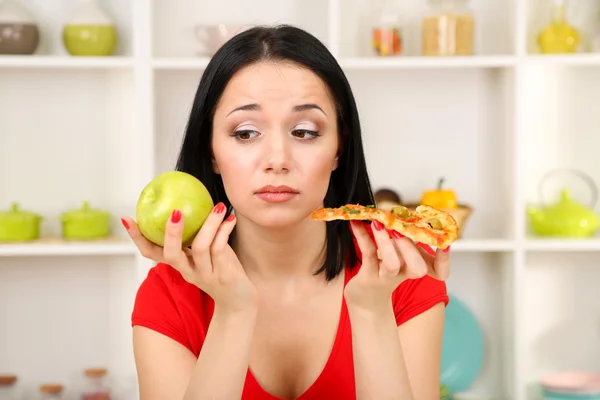 Mooi meisje selecteert pizza of dieet op keuken achtergrond — Stockfoto