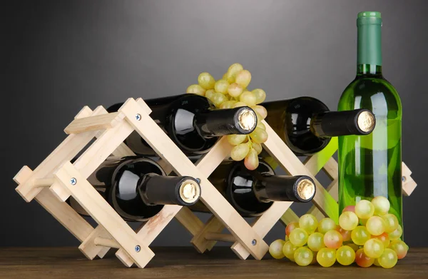 Lahví vína na dřevěný stojan na šedém pozadí — Stock fotografie