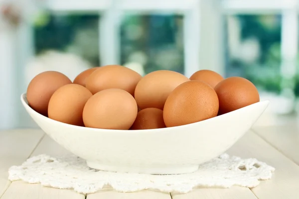 Eieren in witte kom op houten tafel op achtergrond van venster — Stockfoto