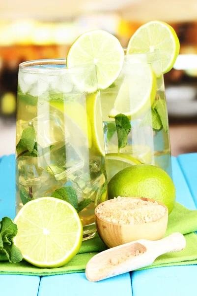 Glasses of cocktail with lime and mint on blue wooden table on bright background — Stock Photo, Image