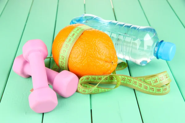 Orange with measuring tape, dumbbells and bottle of water, on color wooden background — Stock Photo, Image